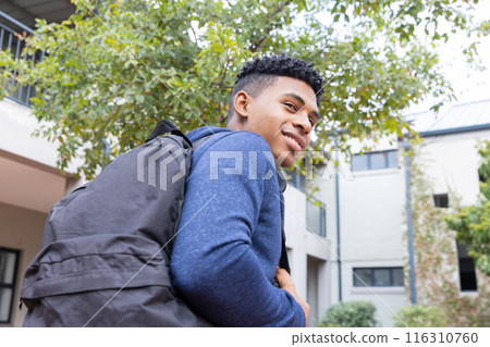 Carrying backpack and smiling, African American male student looking away outdoors at school 116310760