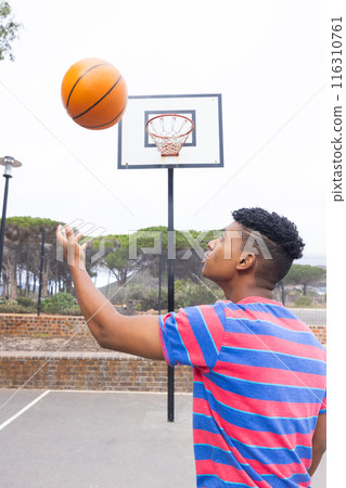 Playing basketball outdoors, teenage boy spinning ball on finger near hoop Playing basketball outdoors, teenage boy spinning ball on finger near hoop 116310761