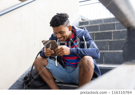 Sitting on stairs, African American teenage boy using tablet, smiling and relaxing Sitting on stairs, African American teenage boy using tablet, smiling and relaxing 116310764
