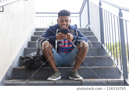 Sitting on stairs, African American teenage boy using smartphone, smiling and relaxing Sitting on stairs, African American teenage boy using smartphone, smiling and relaxing 116310765