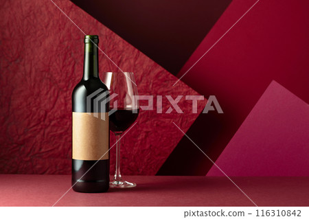 Bottle and glass of red wine on a red background. 116310842