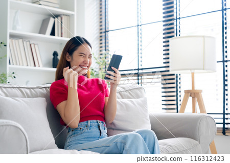 Happy young asian woman relax on comfortable couch at home texting messaging on smartphone Happy young asian woman relax on comfortable couch at home texting messaging on smartphone 116312423