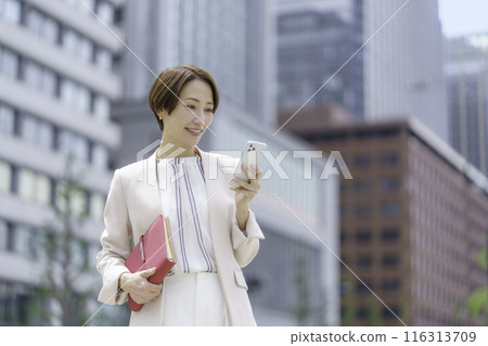 拿著紅色筆記本並在智慧型手機上搜尋的女商人 116313709