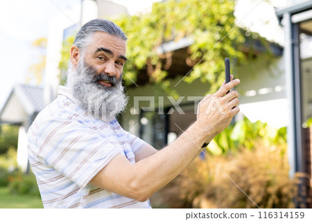 Taking selfie, senior man smiling and holding smartphone outside 116314159
