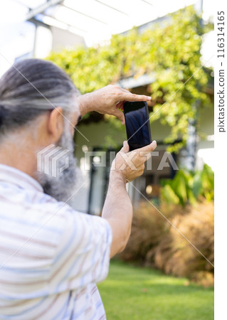 Taking photo with smartphone, senior man capturing outdoor scene in garden, copy space 116314165