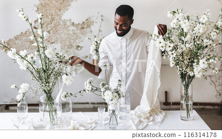 Black wedding designer in white outfits, creating floral decor in a minimalistic loft 116314178