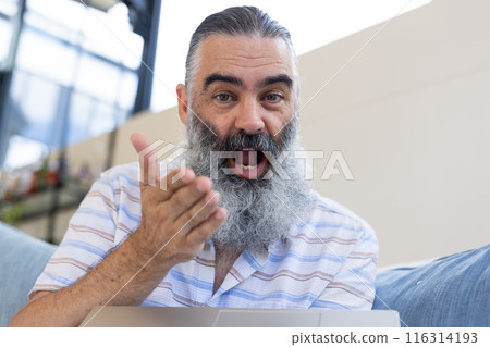 Smiling senior man gesturing while video chatting on laptop at home 116314193