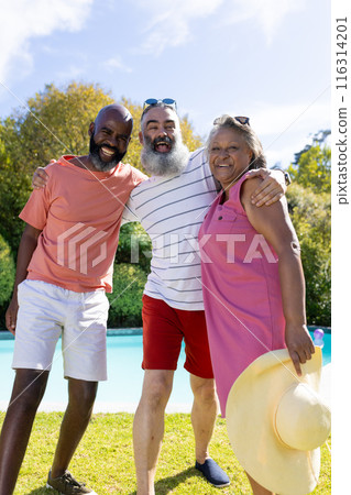 Group of senior friends smiling and embracing outdoors by pool on sunny day 116314201