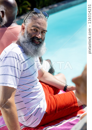 Smiling man with beard sitting by pool with friends, enjoying sunny day Smiling man with beard sitting by pool with friends, enjoying sunny day 116314231