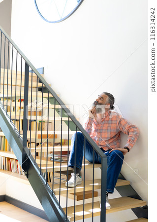 At home, Sitting on stairs, senior man in casual clothes thinking, bookshelf in background 116314242