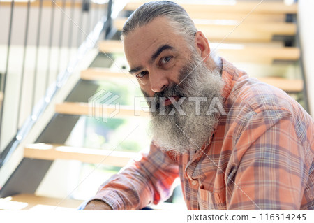 At home, Senior man with long beard sitting on stairs, looking at camera 116314245