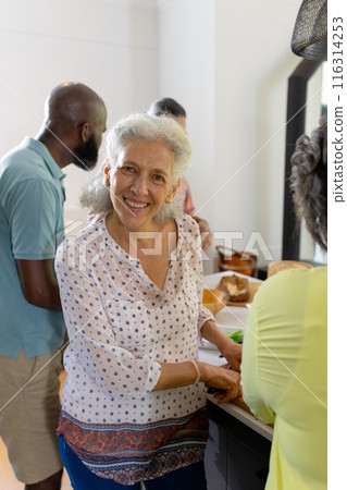 At home, Smiling senior woman preparing food with friends in kitchen, enjoying time together 116314253