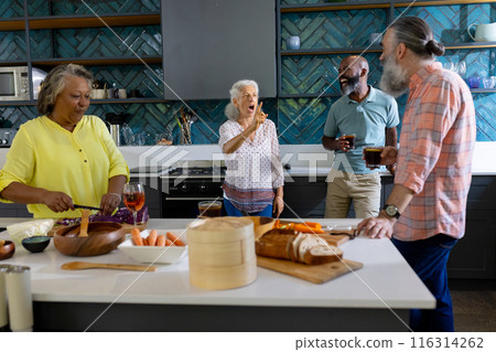 At home, Diverse group of senior friends socializing and preparing food in modern kitchen 116314262