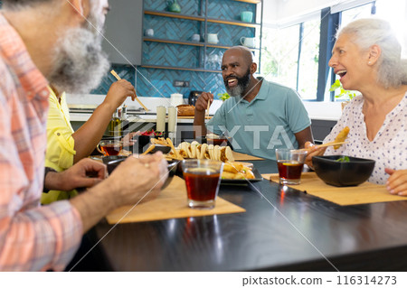 At home, Diverse group of senior friends enjoying meal and laughing together in kitchen At home, Diverse group of senior friends enjoying meal and laughing together in kitchen 116314273