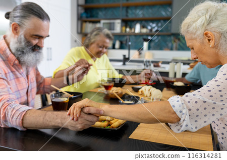 At home, Group of senior friends holding hands and praying before meal in kitchen 116314281