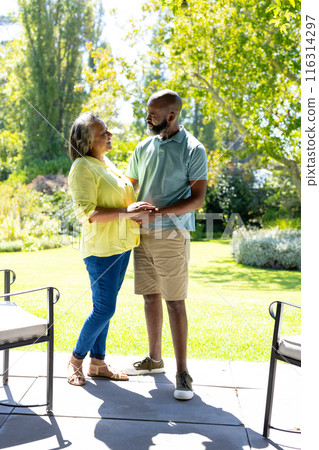 Senior couple holding hands and smiling at each other in sunny garden 116314297