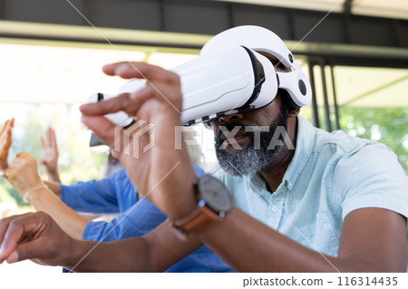 Using VR headset, senior man exploring virtual reality with friends Using VR headset, senior man exploring virtual reality with friends 116314435
