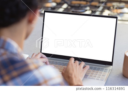 Using laptop with blank screen, teenage boy typing at home with coffee mug, copy space 116314891