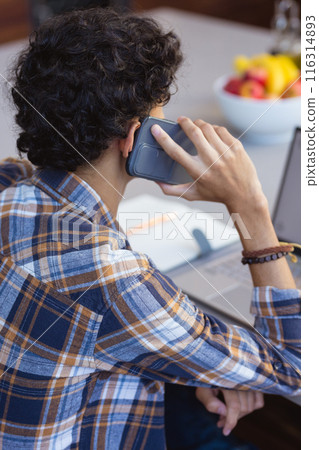 Talking on smartphone, teenage boy working on laptop at home office desk Talking on smartphone, teenage boy working on laptop at home office desk 116314893