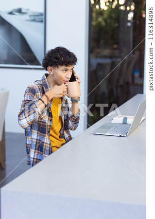 Talking on smartphone and drinking coffee, teenage boy working on laptop at home, copy space Talking on smartphone and drinking coffee, teenage boy working on laptop at home, copy space 116314898