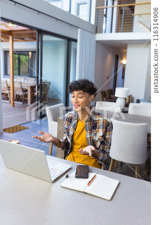 Using laptop and gesturing, teenage boy video conferencing from home office setup 116314906