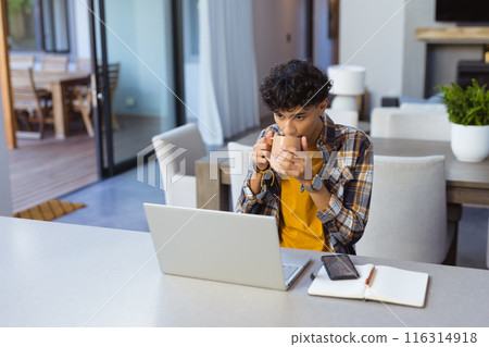 Drinking coffee, teenage boy using laptop and smartphone at home office 116314918