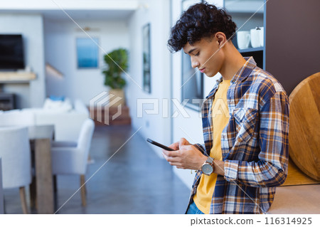 Using smartphone, teenage boy standing in modern home, focusing on screen, copy space 116314925