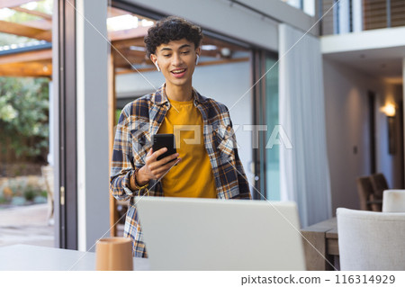 Using smartphone and laptop, teenage boy multitasking in modern home environment 116314929