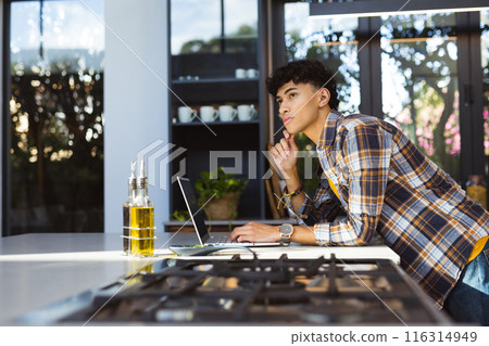 Using laptop in modern kitchen, teenage boy thinking and working, copy space Using laptop in modern kitchen, teenage boy thinking and working, copy space 116314949