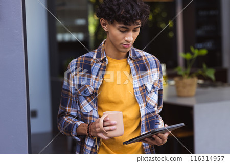 Holding tablet and drinking coffee, teenage boy standing in modern kitchen Holding tablet and drinking coffee, teenage boy standing in modern kitchen 116314957