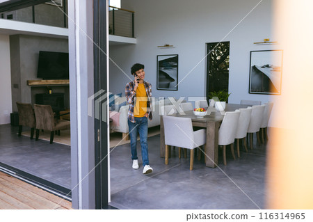 Talking on smartphone, young man walking through modern living room at home 116314965