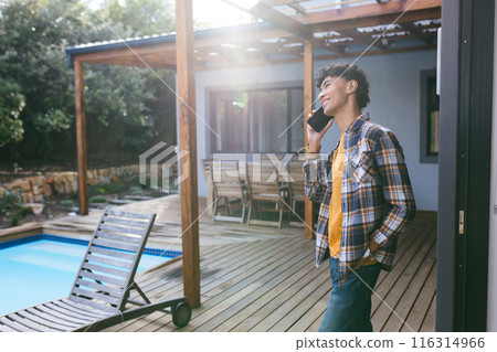 Talking on smartphone, teenage boy standing on wooden deck by swimming pool Talking on smartphone, teenage boy standing on wooden deck by swimming pool 116314966