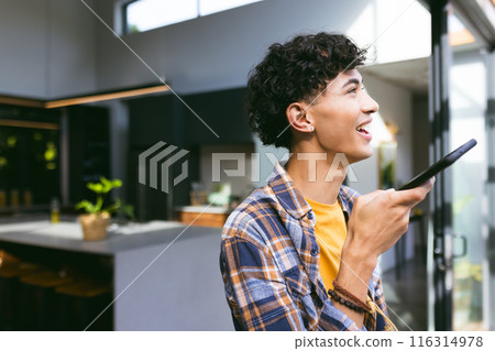 Holding smartphone, teenage boy smiling and speaking in modern home setting Holding smartphone, teenage boy smiling and speaking in modern home setting 116314978