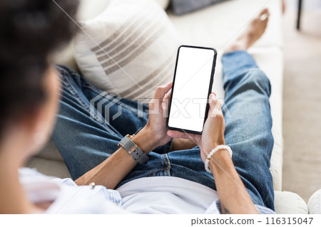 Holding smartphone with blank screen, teenage boy relaxing on couch at home 116315047