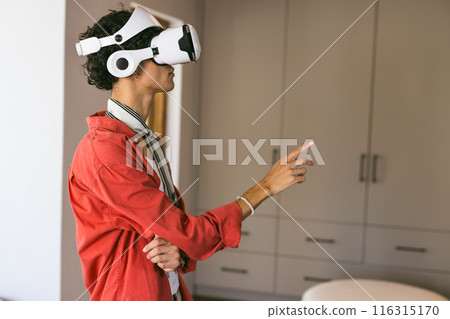Using VR headset, young man pointing and interacting with virtual environment at home 116315170