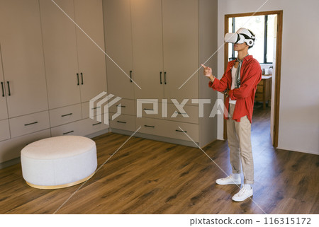Using VR headset, young man exploring virtual environment in modern home setting 116315172
