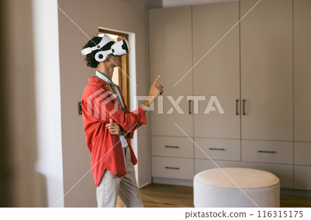 Using VR headset, young man exploring virtual environment in modern home setting Using VR headset, young man exploring virtual environment in modern home setting 116315175