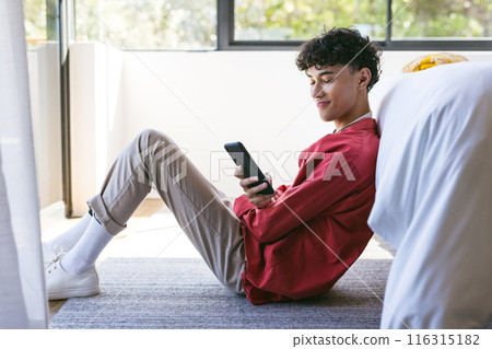Sitting on floor, teenage boy using smartphone and smiling at home Sitting on floor, teenage boy using smartphone and smiling at home 116315182