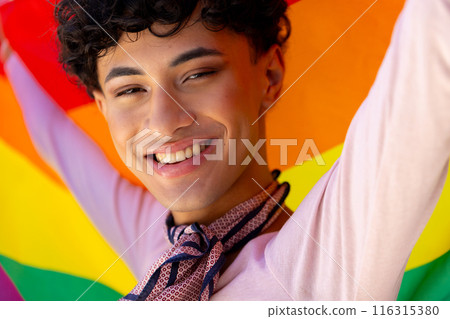 Smiling young man holding rainbow flag, celebrating LGBTQ+ pride and diversity 116315380