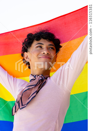 Holding rainbow flag, young man smiling and celebrating LGBTQ+ pride outdoors 116315381