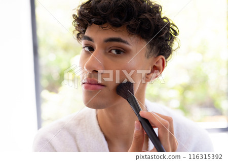 Applying makeup, young man using brush for contouring at home, focusing on face Applying makeup, young man using brush for contouring at home, focusing on face 116315392