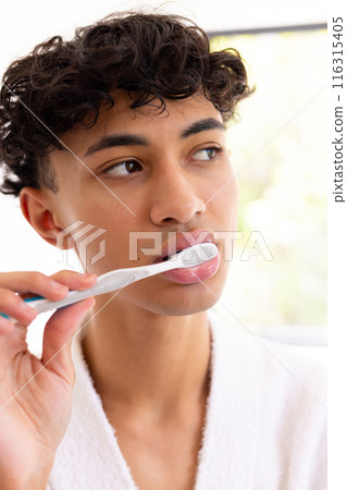 Brushing teeth, young young man in white robe focusing on oral hygiene 116315405