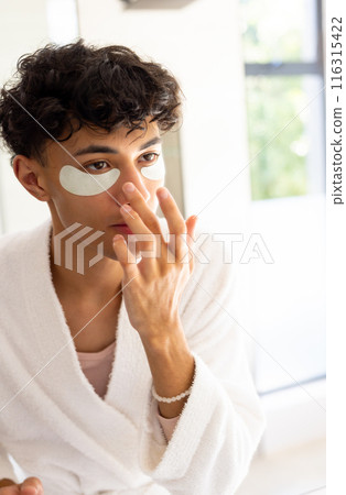 Applying skincare, young young man with eye patches in bathroom, wearing bathrobe 116315422