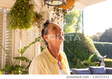 Smiling mature woman enjoying sunny day in cozy home garden patio 116315512