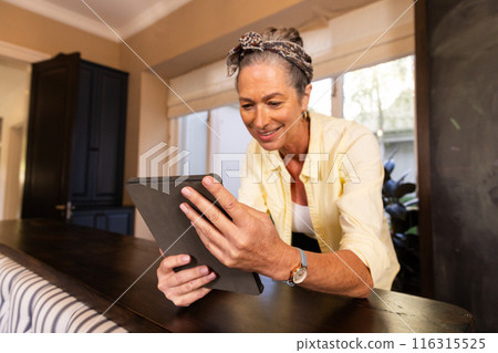 Using tablet, mature woman smiling and working from home in kitchen Using tablet, mature woman smiling and working from home in kitchen 116315525