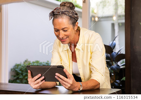 Smiling senior woman using tablet while standing at home, enjoying technology Smiling senior woman using tablet while standing at home, enjoying technology 116315534