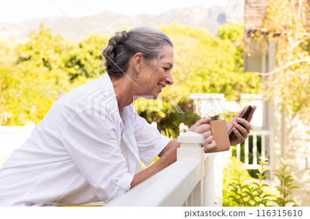 Smiling senior woman holding smartphone and coffee cup, enjoying outdoor relaxation Smiling senior woman holding smartphone and coffee cup, enjoying outdoor relaxation 116315610