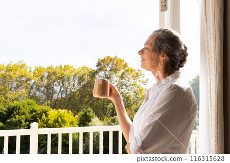 Holding coffee mug, mature woman enjoying morning view from balcony, copy space Holding coffee mug, mature woman enjoying morning view from balcony, copy space 116315628