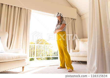 Using VR headset, woman standing in bright living room, exploring virtual reality Using VR headset, woman standing in bright living room, exploring virtual reality 116315634