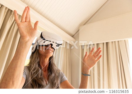 Using VR headset, mature woman experiencing virtual reality at home 116315635
